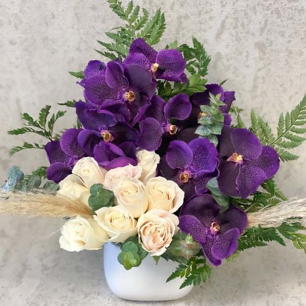 Purple orchids and cream roses in a white vase