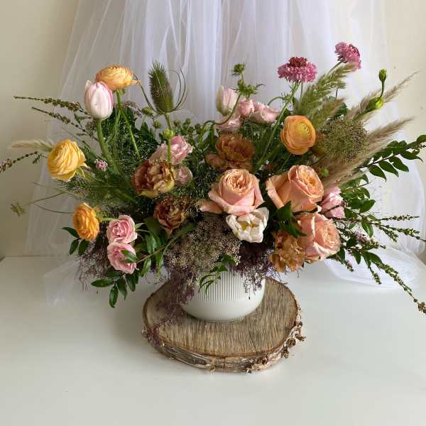 Mixed bouquet of peach, pink, and yellow flowers in a white vase