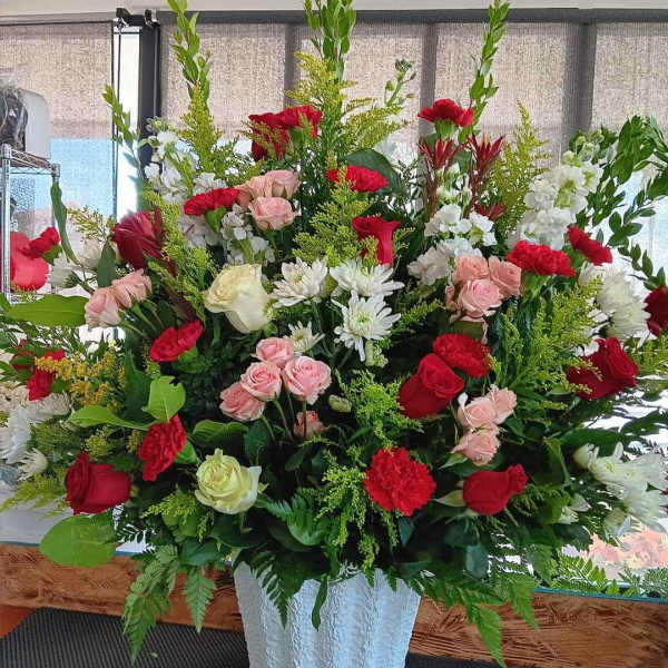 Large mixed flower arrangement in a white vase with red, pink, and white blooms