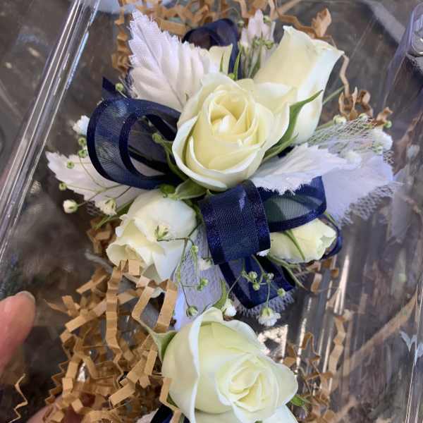 White rose corsage with navy ribbon in clear packaging