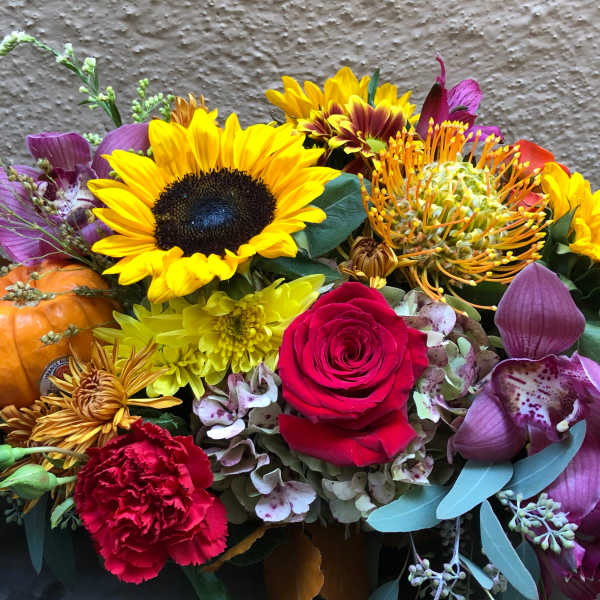 Mixed floral arrangement with sunflowers, roses, orchids, and a small pumpkin