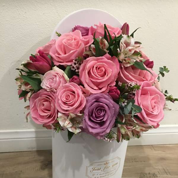Pink and purple roses arranged in a white hatbox