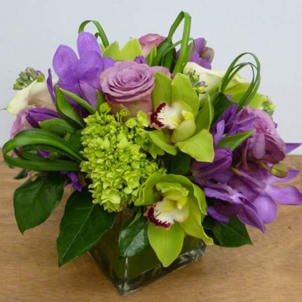 Purple and green floral arrangement in a square glass vase