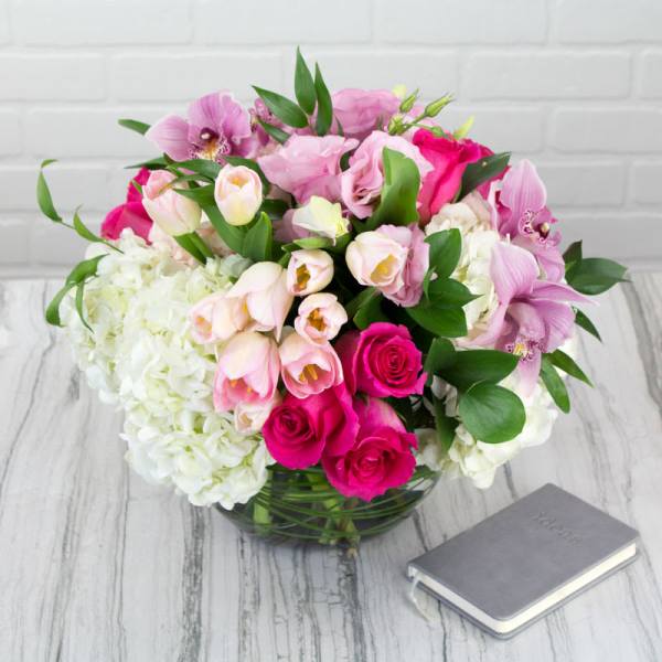 Pink and white mixed bouquet in a glass vase beside a small book