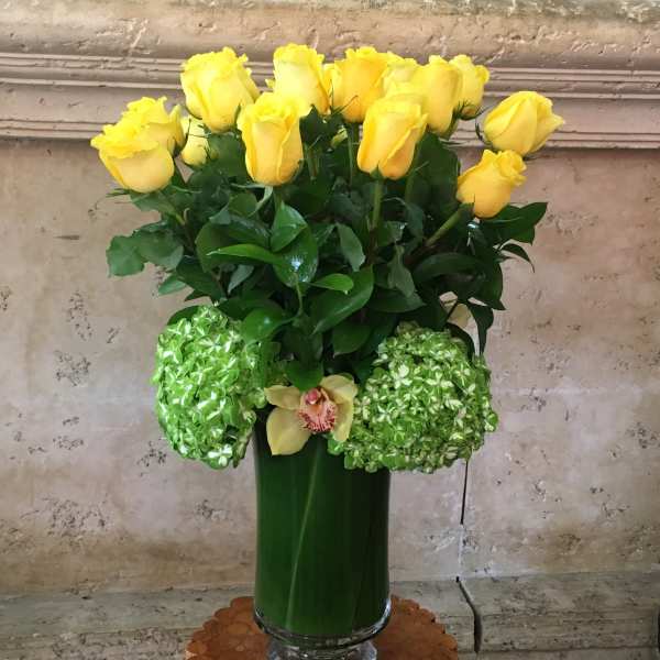 Yellow roses and green hydrangeas in a tall glass vase