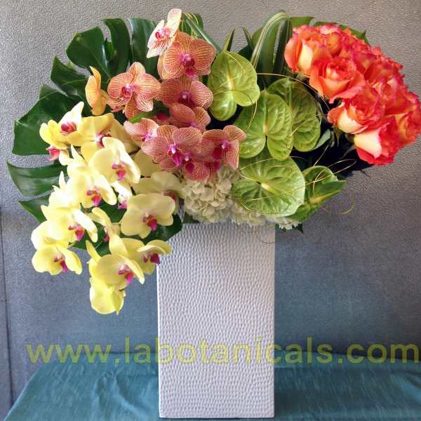 Tropical floral arrangement with orchids and roses in a white vase