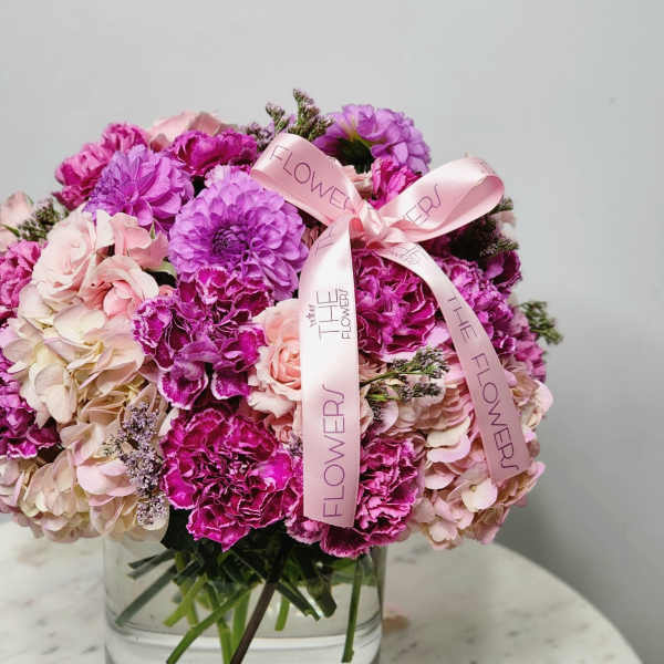 Pink and purple flower arrangement in a clear glass vase with a ribbon