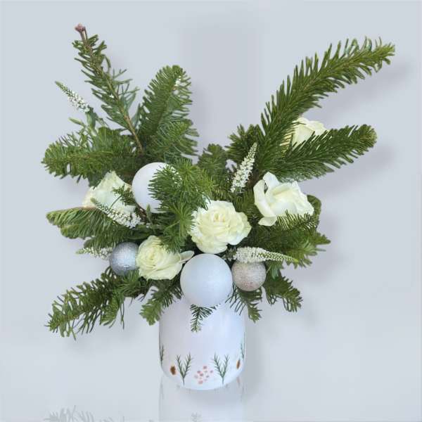 White roses and evergreen branches arranged in a decorated vase with silver ornaments