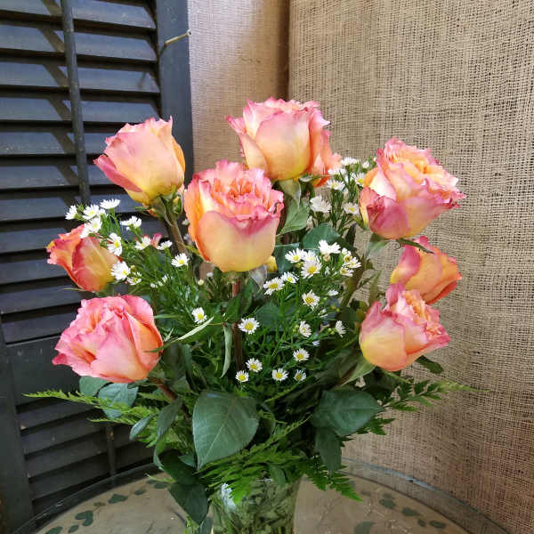Pink and yellow roses with small white daisies in a glass vase