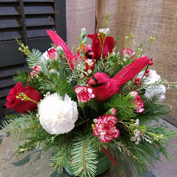 Holiday arrangement with red cardinals, roses, and white carnations in a green vase