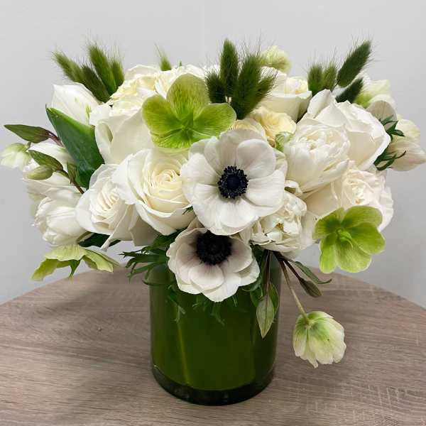 Compact arrangement of white roses and anemones with green blooms in a dark green glass vase