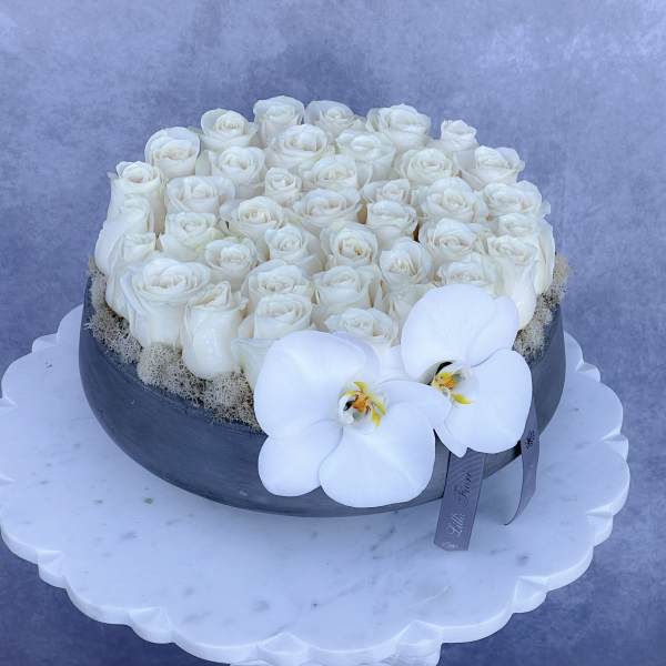 White roses arranged in a round black box with white orchids on the front.