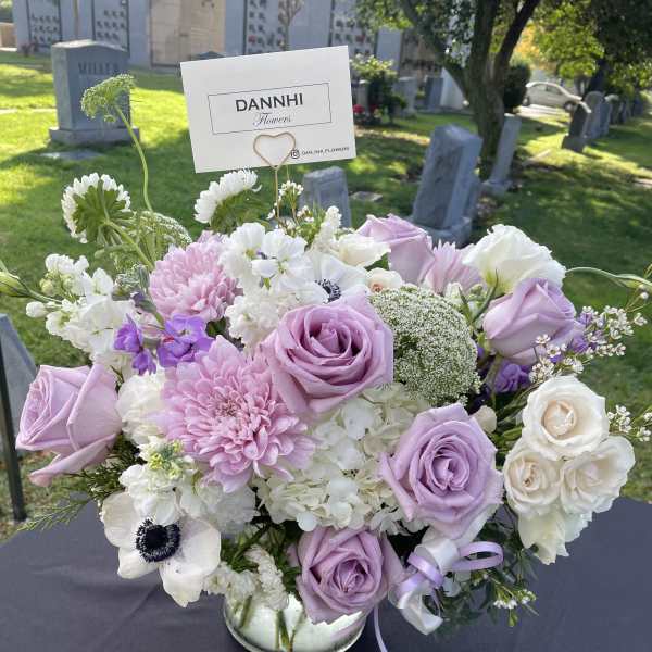 Lavender and white floral arrangement in a glass vase with a card pick