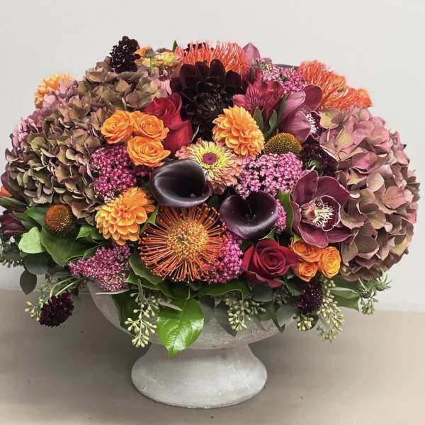 Mixed floral arrangement in a gray pedestal vase with pink, orange, and dark blooms