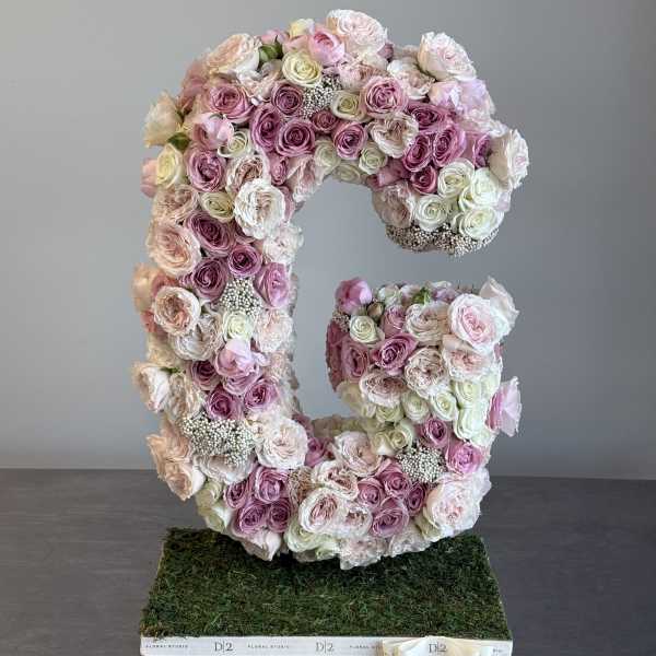 Large floral letter C made of pink and white roses on a moss base