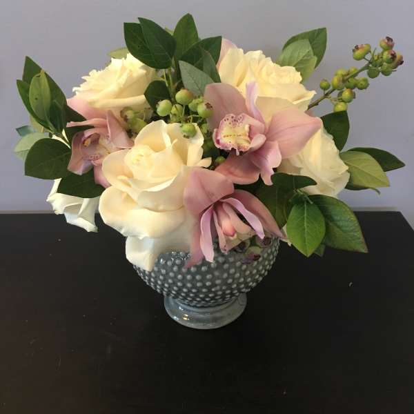 Cream roses and pink orchids arranged in a dotted glass vase