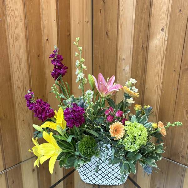 Colorful mixed flower arrangement in a white patterned ceramic container.