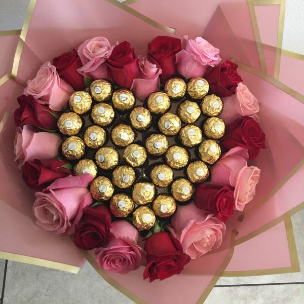 Heart-shaped bouquet of pink and red roses with gold-wrapped chocolates