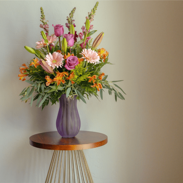 Mixed pink and orange flower arrangement in a purple vase