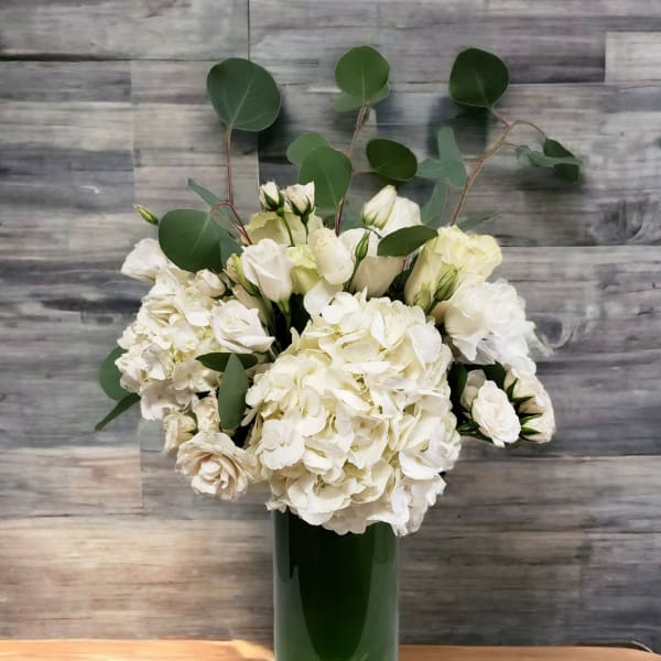 White flowers arranged in a tall green vase with round eucalyptus stems