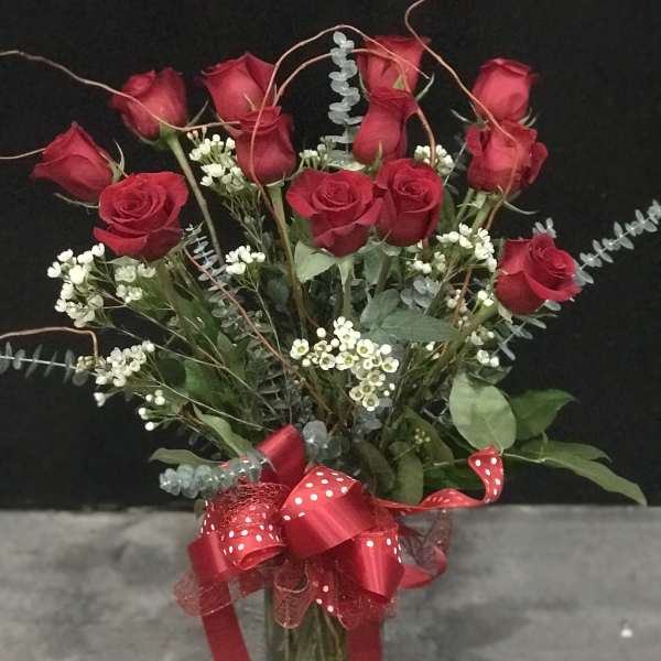Red roses arranged in a glass vase with a red ribbon bow