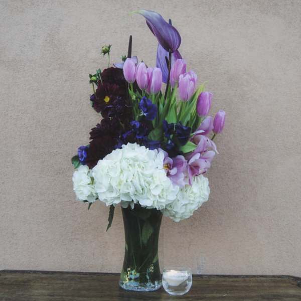 Tall bouquet of pink tulips, purple flowers, and white hydrangeas in a glass vase