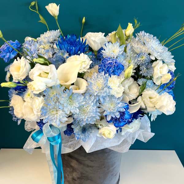 Blue and white floral arrangement in a gray hatbox with ribbon
