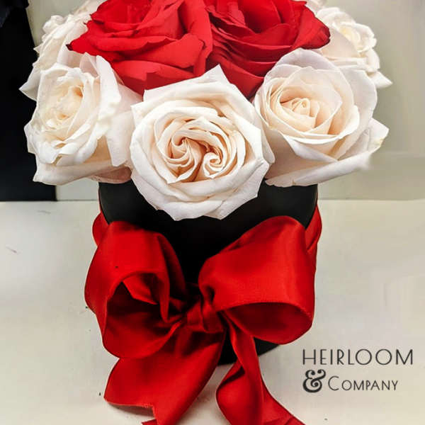 Red and white roses arranged in a black hat box with a red ribbon