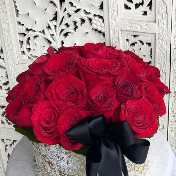 Red roses arranged in a round gold-patterned box with a black ribbon