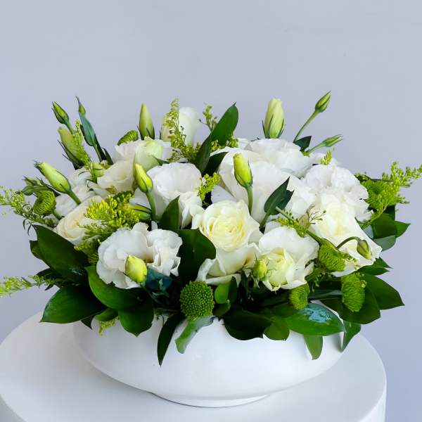 White floral arrangement in a low white vase with green accents
