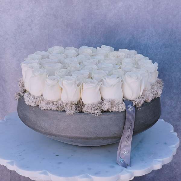 Round arrangement of white roses in a gray bowl with a ribbon