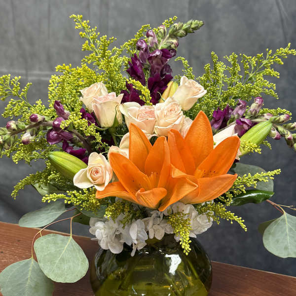 Orange lilies and pale roses in a green glass vase