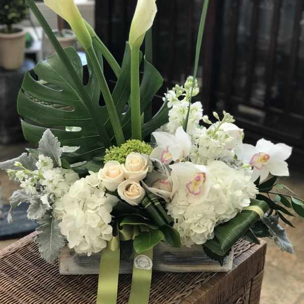White floral arrangement with calla lilies, roses, and orchids in a wooden box