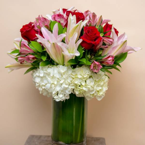 Bouquet of red roses, pink lilies, and white hydrangeas in a glass vase