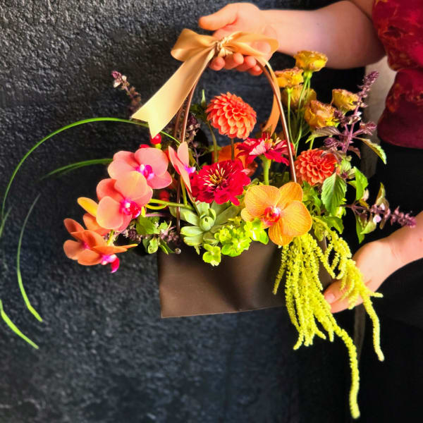 Handheld basket arrangement with orchids and bright mixed flowers