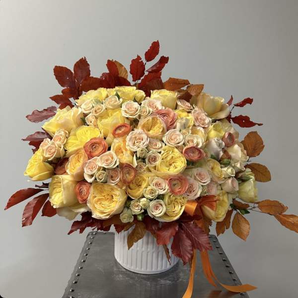 Large bouquet of yellow and peach roses in a white vase with autumn leaves