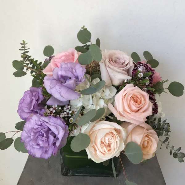 Bouquet of pink, peach, and lavender roses with eucalyptus in a square vase