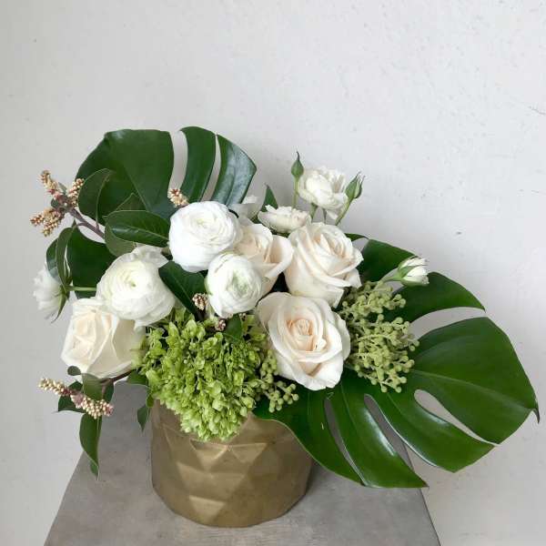 White roses and ranunculus in a gold vase with large tropical leaves