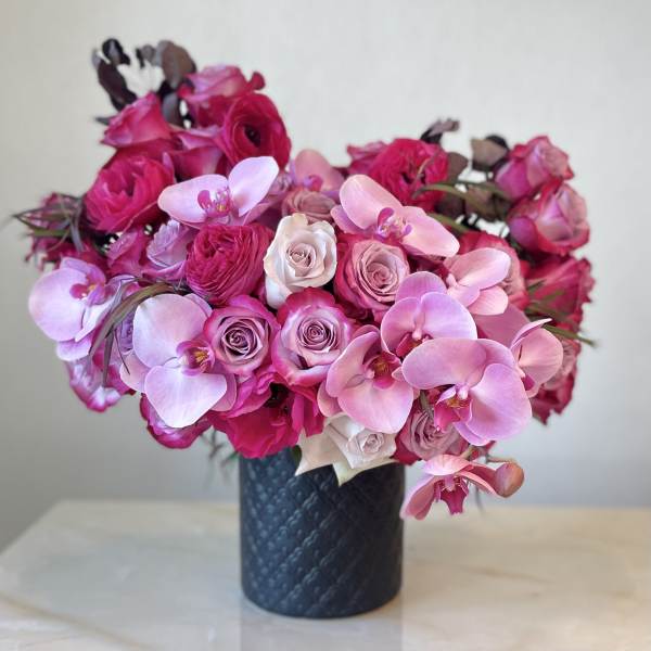 Pink roses and orchids arranged in a dark vase