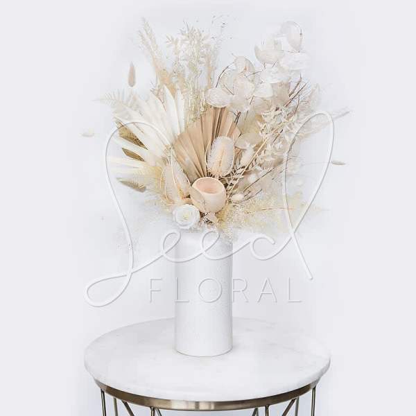 Cream dried floral arrangement in a white vase on a round table