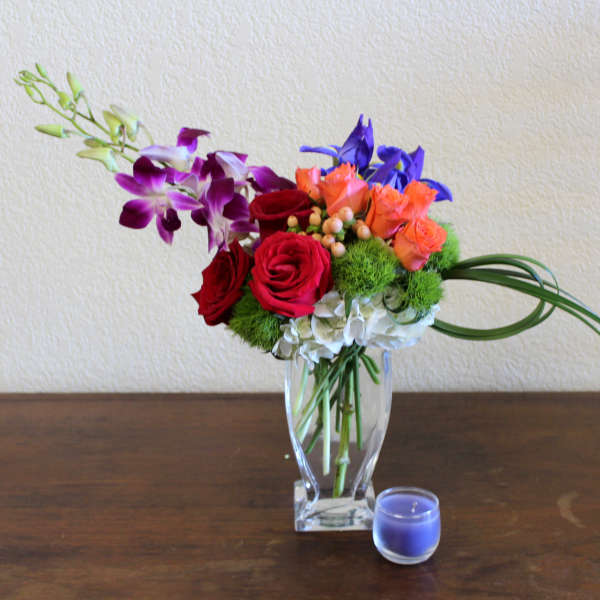 Mixed bouquet of roses and orchids in a clear glass vase with a small blue candle