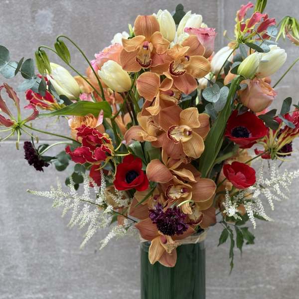 Mixed bouquet with orange orchids, red anemones, and pale tulips in a green vase