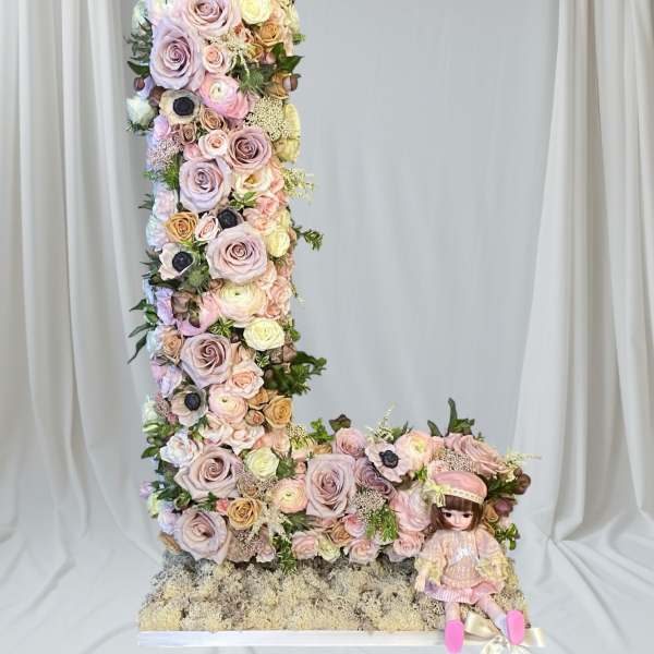 Tall floral letter L with pastel roses and a doll at the base