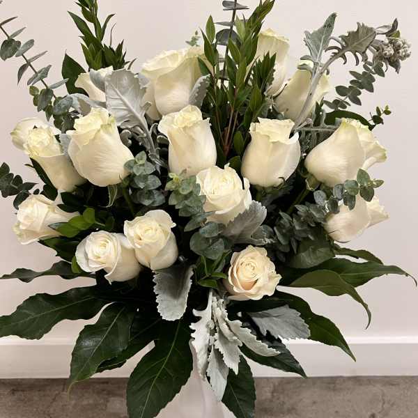 White roses arranged in a tall white vase with silver-green foliage