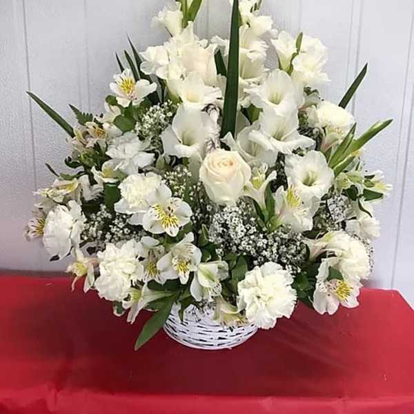 White floral arrangement in a white basket with tall blooms and greenery