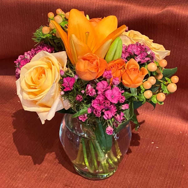 Orange and cream roses with pink filler flowers in a glass vase