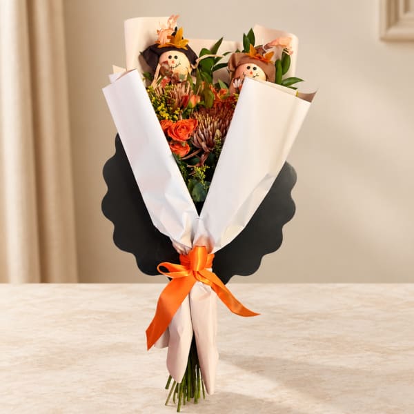 Bouquet of orange flowers with two small scarecrow decorations and an orange ribbon