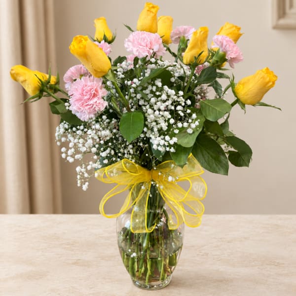 Yellow roses and pink carnations in a glass vase with a yellow ribbon