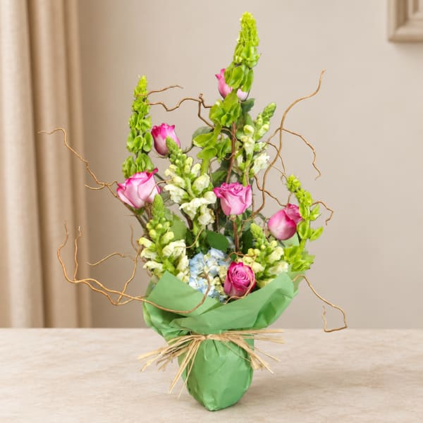 Pink roses and snapdragons in a green wrapped vase arrangement