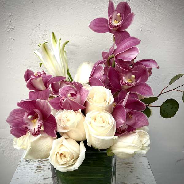 Pink orchids and white roses arranged in a clear square vase